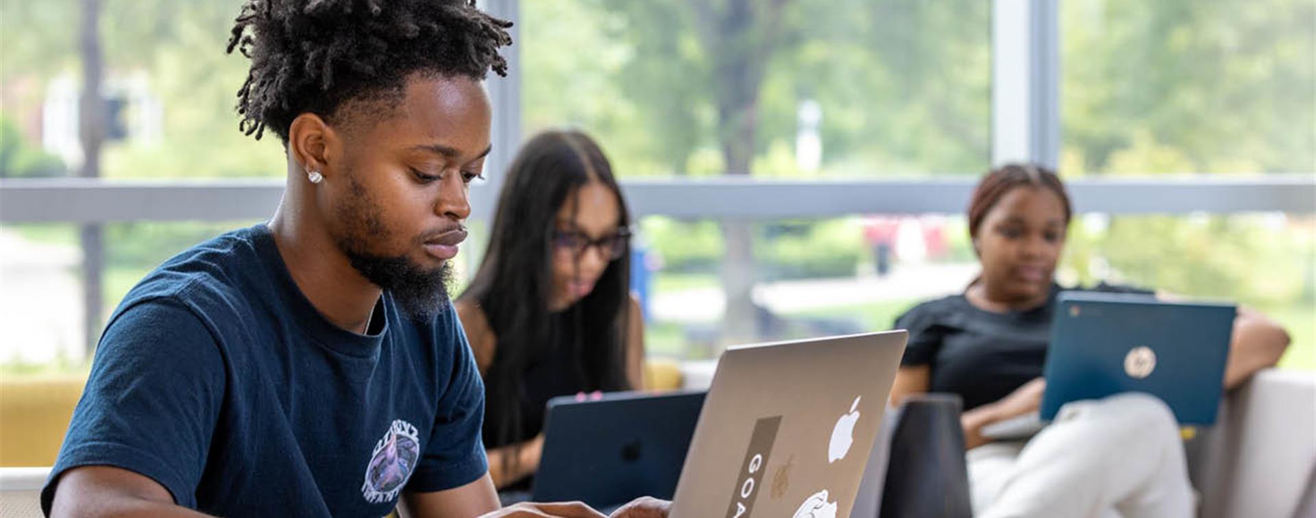 Three college students sitting in a lounge and working on their laptops