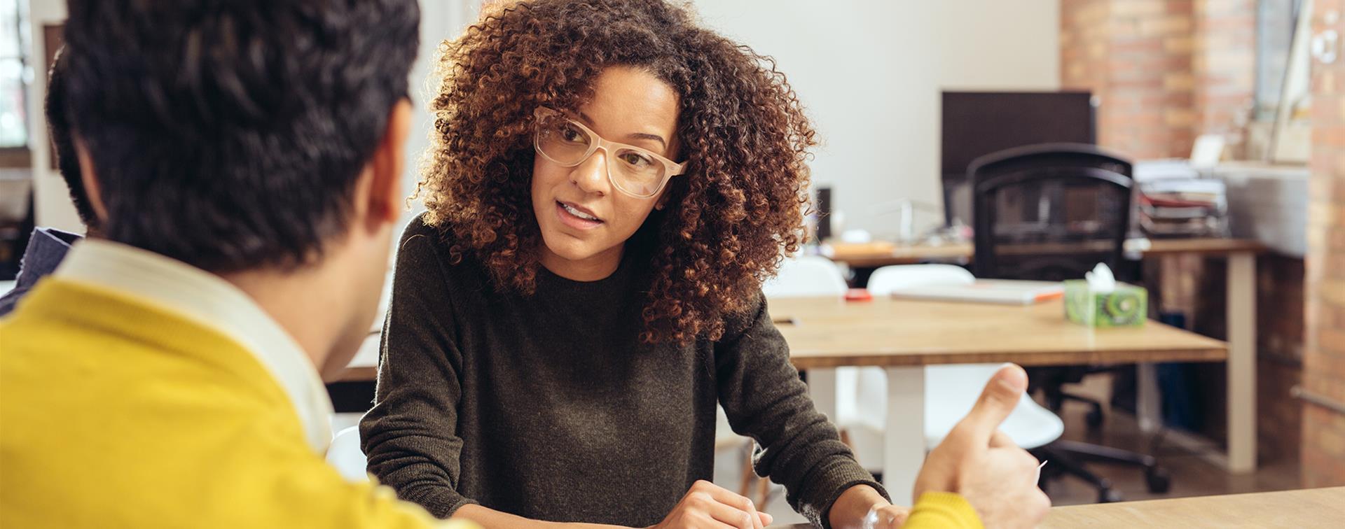 A woman sits at a desk and looks compassionately at a person she is having a conversation with