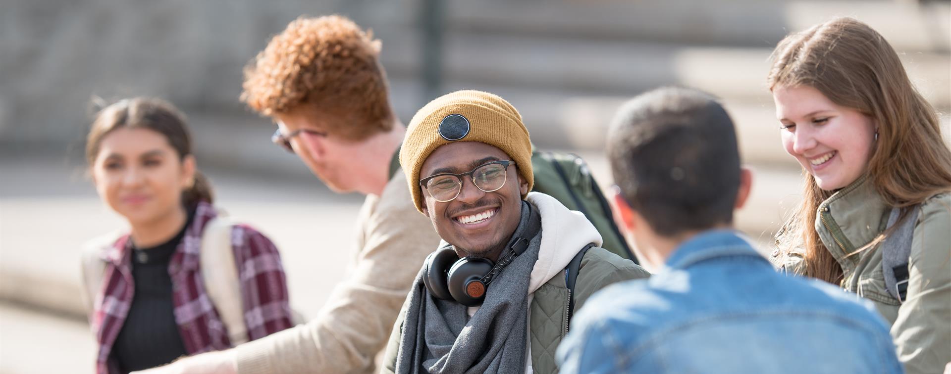 A group of students sit outside on stone steps, smiling and laughing.