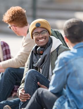 A group of students sit outside on stone steps, smiling and laughing.