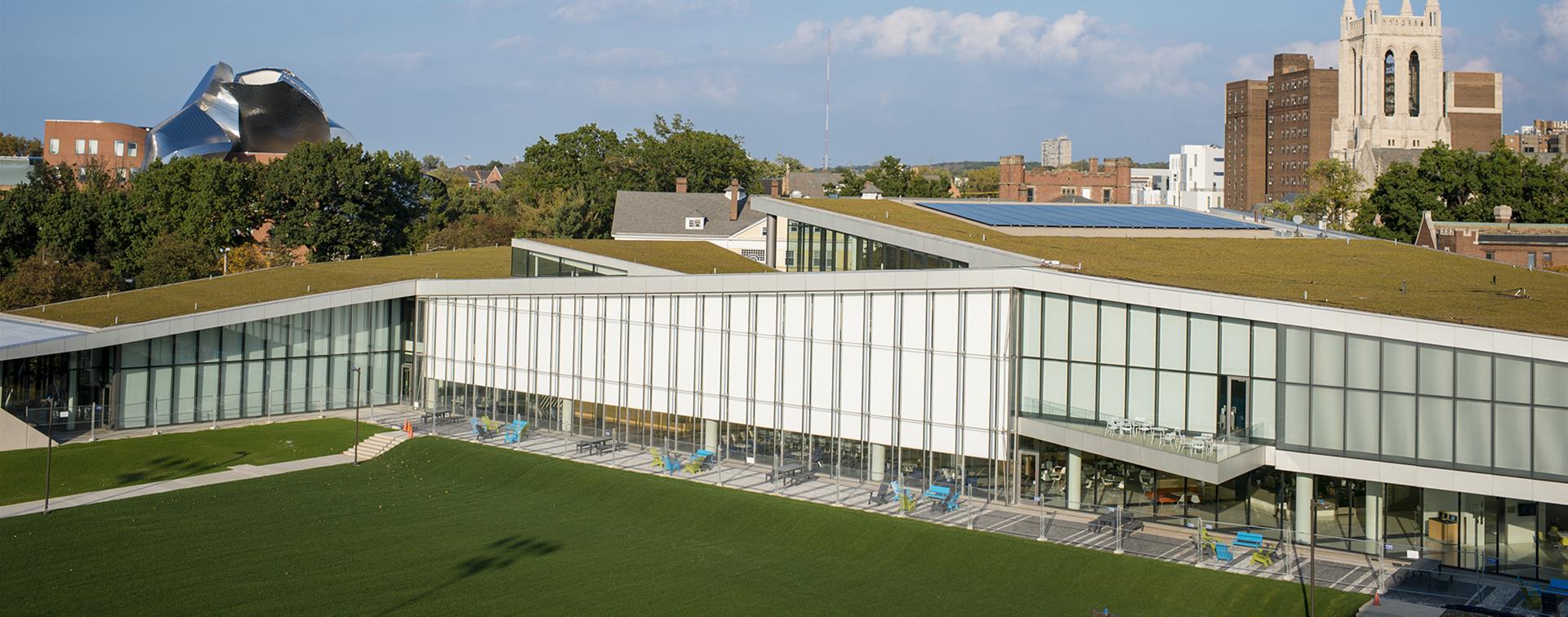 Photo of a modern building on a college campus that has solar panels and grass on its roof.