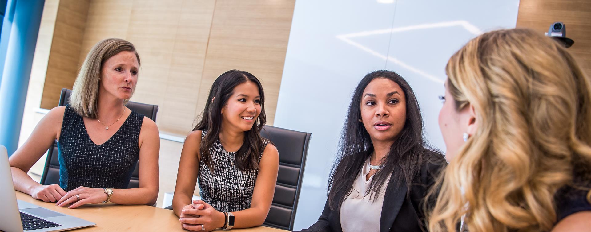 A picture of women sitting around a table dressed in business attire for a meeting