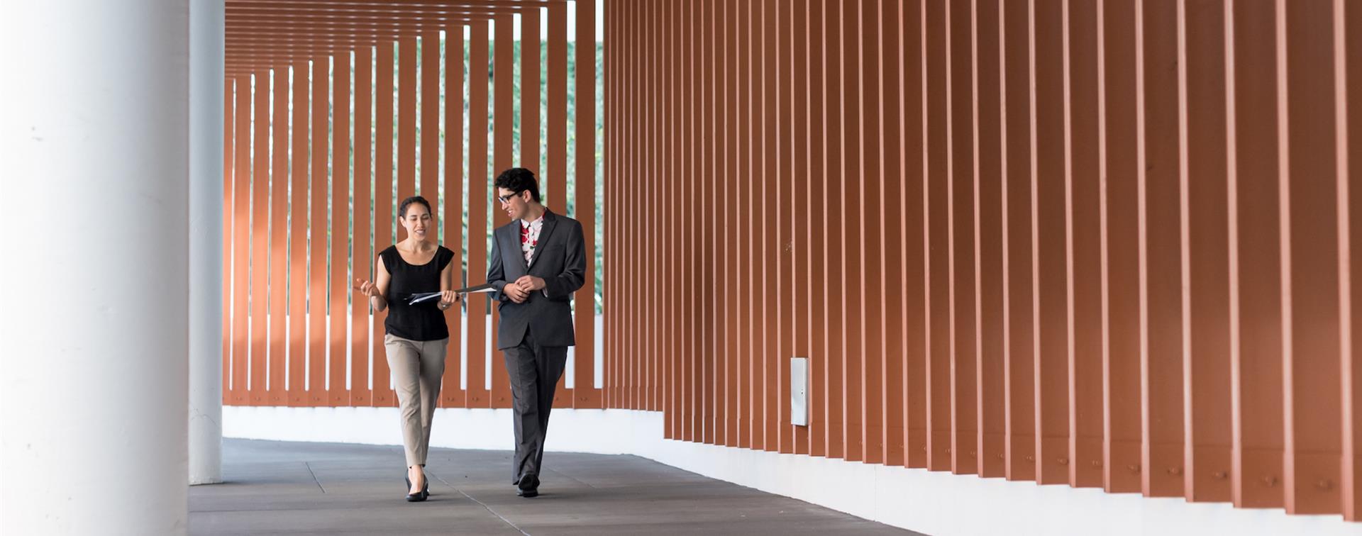 Picture of two colleagues walking down a hallway and collaborating. 