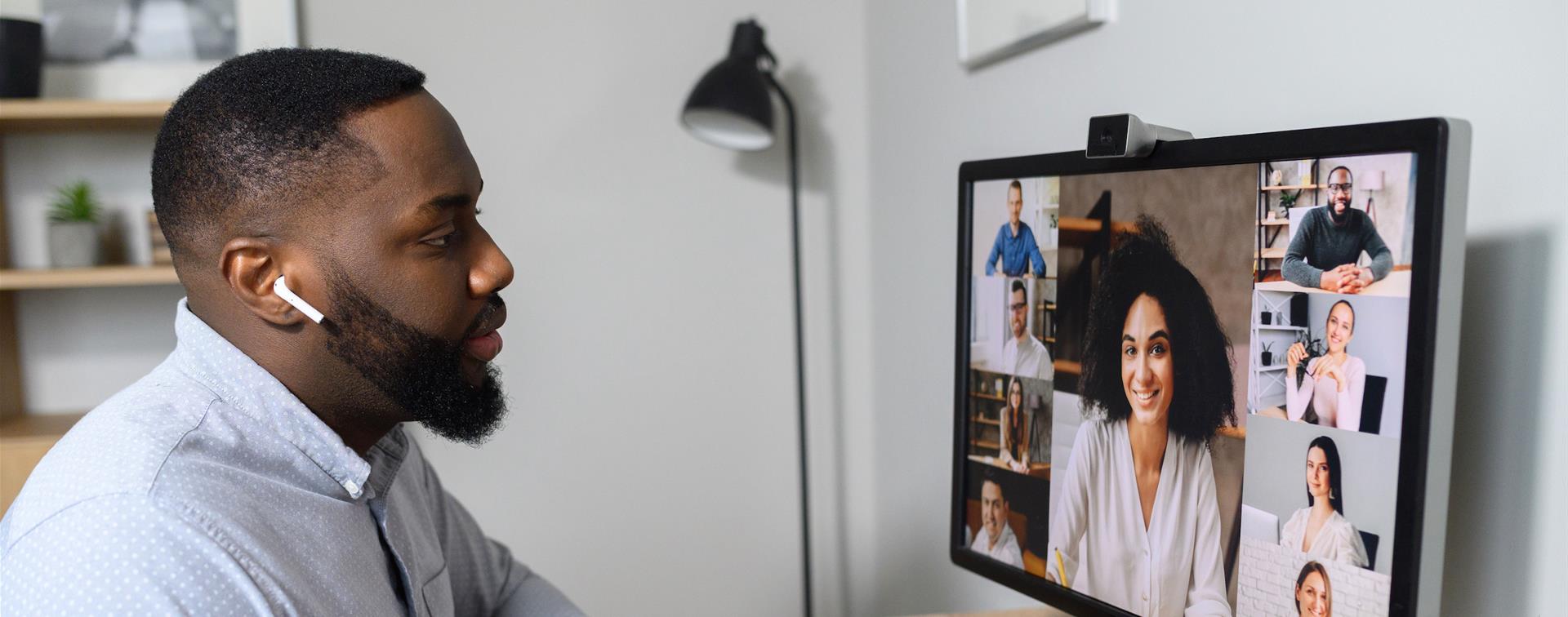 Photo of young man at computer screen participating in virtual meeting