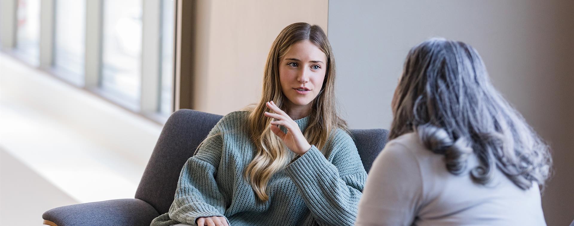 Two women sit across from each other, one speaks while the other listens intently.